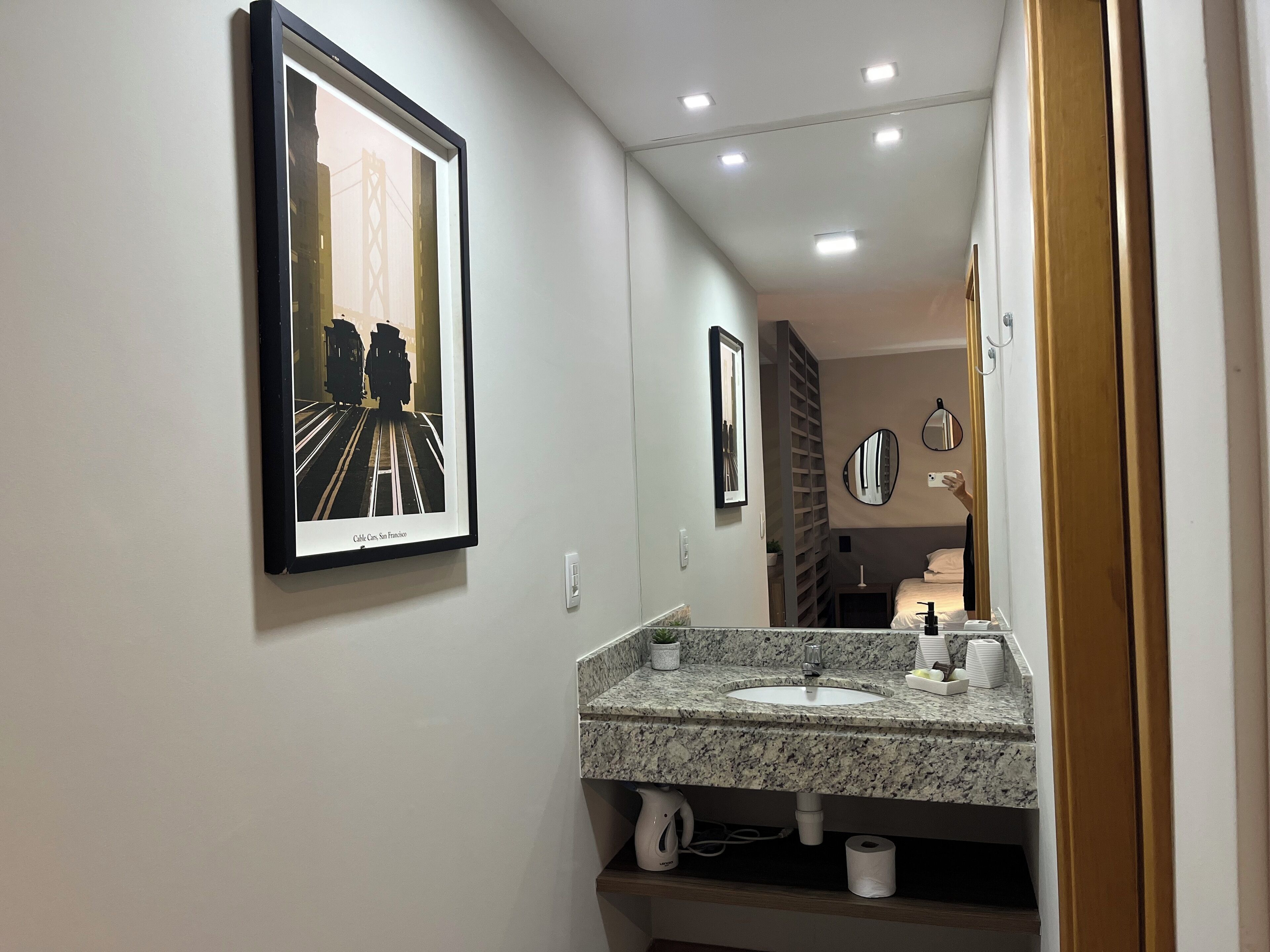A modern bathroom with a granite countertop sink, a framed picture of a train, and a mirror.