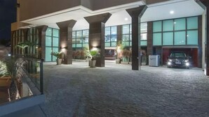 Une entrée d’hôtel moderne avec un espace extérieur abrité, de grandes fenêtres et un parking.
