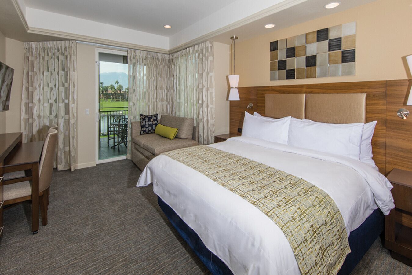A hotel room with a large bed, a sofa, a desk, and a balcony with a view of the mountains.