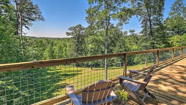 Eine Holzdielen-Terrasse mit Adirondack-Stühlen mit Blick auf eine von einem Zaun umfriedete, begrünte Fläche mit Bäumen.