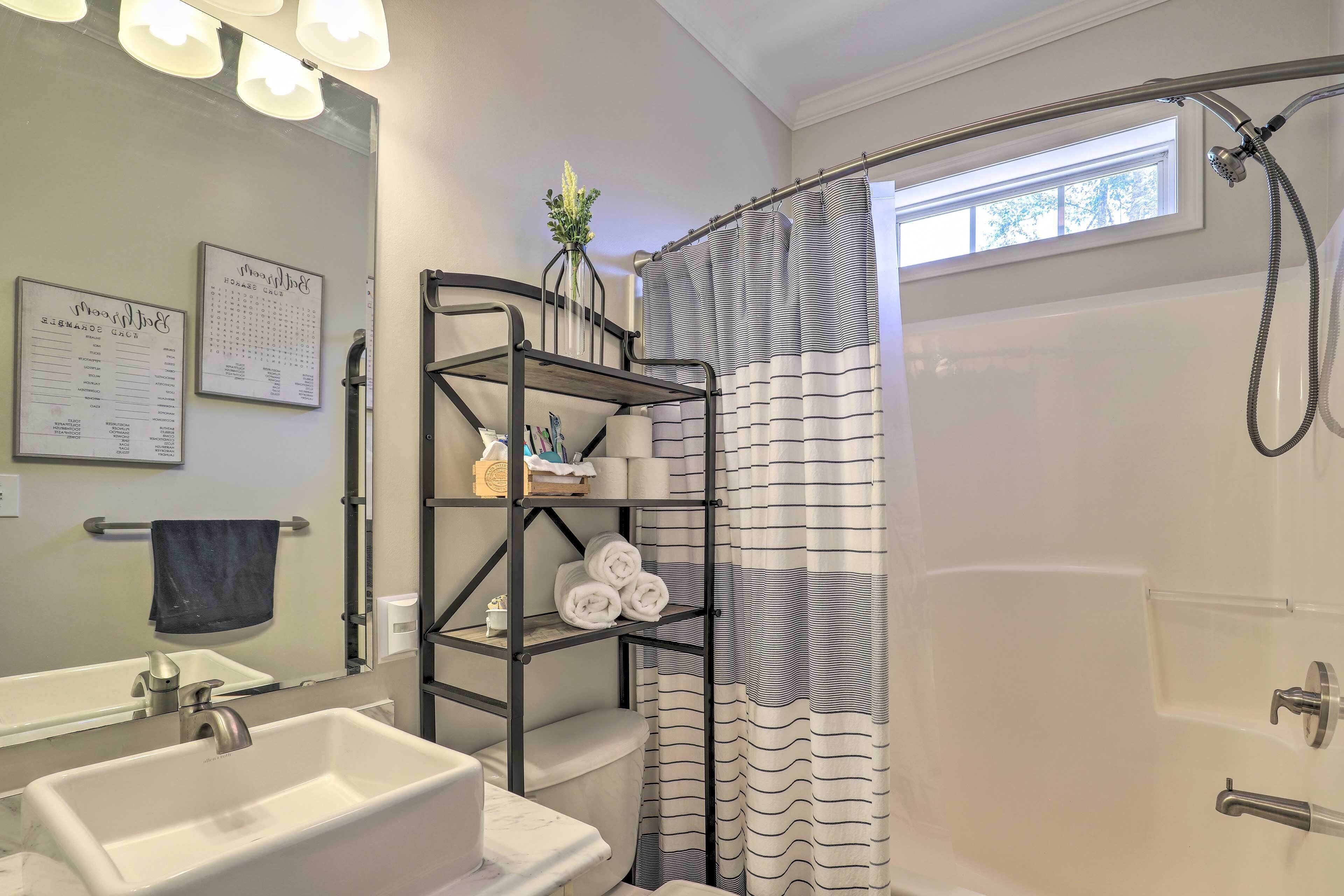 A bathroom with a white sink, a mirror, a shower with a striped curtain, and a towel rack with towels.