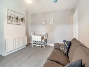 A living room with a white table and chairs, a brown sofa, and a radiator. - Bluebell Apartment - UK42381 (Bridlington)