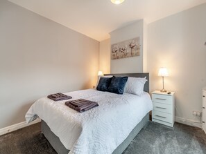 A neatly made bed with a white duvet, two pillows, and folded towels on a grey carpeted floor. - Bluebell Apartment - UK42381 (Bridlington)
