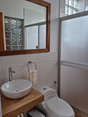 A bathroom with a wooden vanity, a white sink, a mirror, a towel rack, and a toilet.
