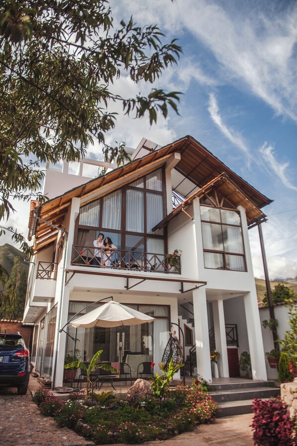 A two-story house with a balcony, a covered patio, and a garden.