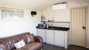 A compact living space with a kitchenette, a brown leather sofa, and a door with a handle. - Coltsfoot Country Retreat (Knebworth)
