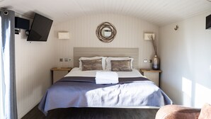 A bedroom with a bed, a flat-screen TV mounted on the wall, a mirror, and a small table with a vase. - Coltsfoot Country Retreat (Knebworth)