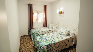 A room with two beds, a window with curtains, and a small wall decoration. - .................... (AN)