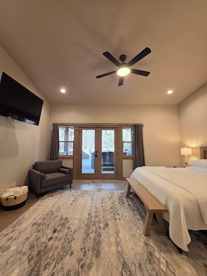 A hotel room with a bed, a chair, a television, a ceiling fan, and a view through the glass doors.