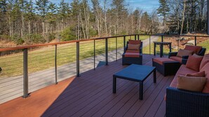 A deck with outdoor furniture, a railing, and a view of a forested area.