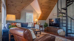 A cozy living room with a leather sofa, a television, and a staircase.