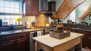 A kitchen with dark wooden cabinets, a stone backsplash, a central island, and a window with blinds.