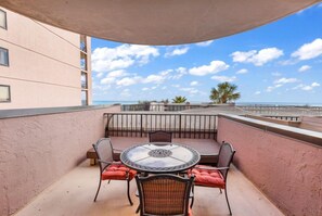Eine Terrasse im Freien mit einem runden Tisch und Stühlen, einer gepolsterten Bank und Blick auf den Ozean.
