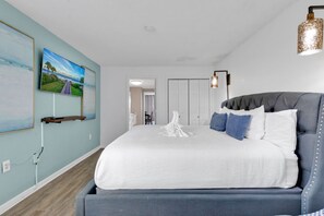 Ein Schlafzimmer mit einem großen Bett, einem Nachttisch, einem Wandregal mit einem Gemälde und einer Tür zu einem anderen Raum.