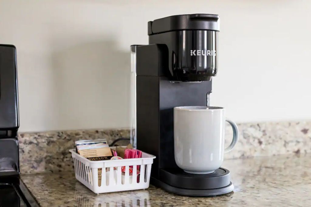 A Keurig coffee maker on a kitchen counter with a basket of coffee pods and a white mug.