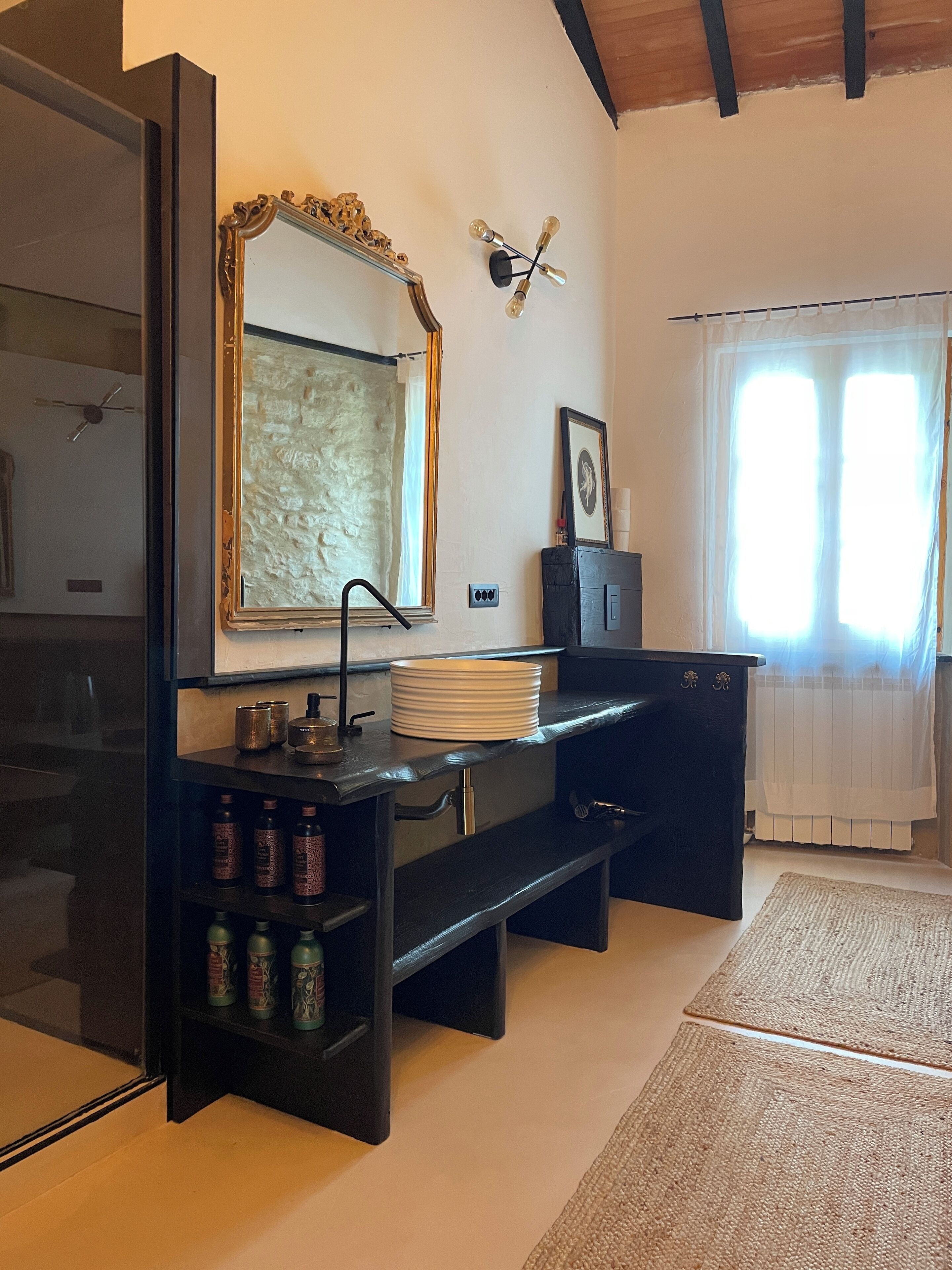 A modern kitchen with a black countertop, a large mirror, and a window with sheer curtains.