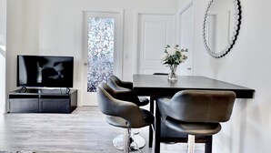 Un salon moderne doté d’un téléviseur à écran plat, d’une table à manger avec des chaises, d’un grand miroir et d’une porte ornée d’un vitrail.