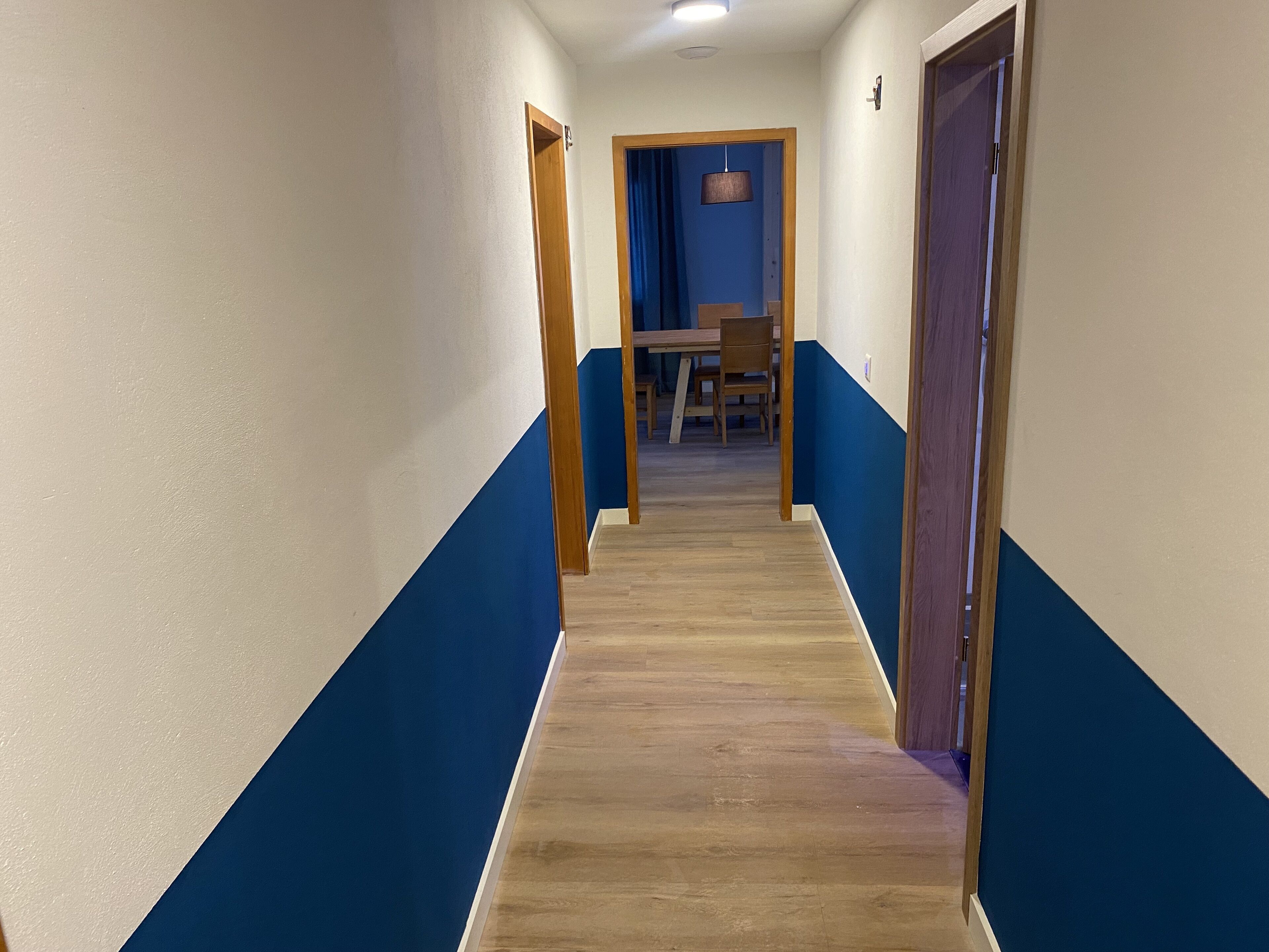 Un corridoio con pareti blu e bianche, pavimento in legno e un tavolo con sedie sullo sfondo.