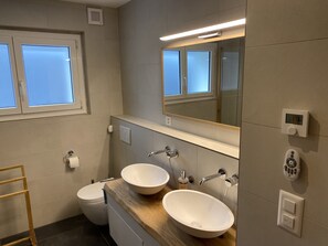 A modern bathroom with two sinks, a toilet, and a window.