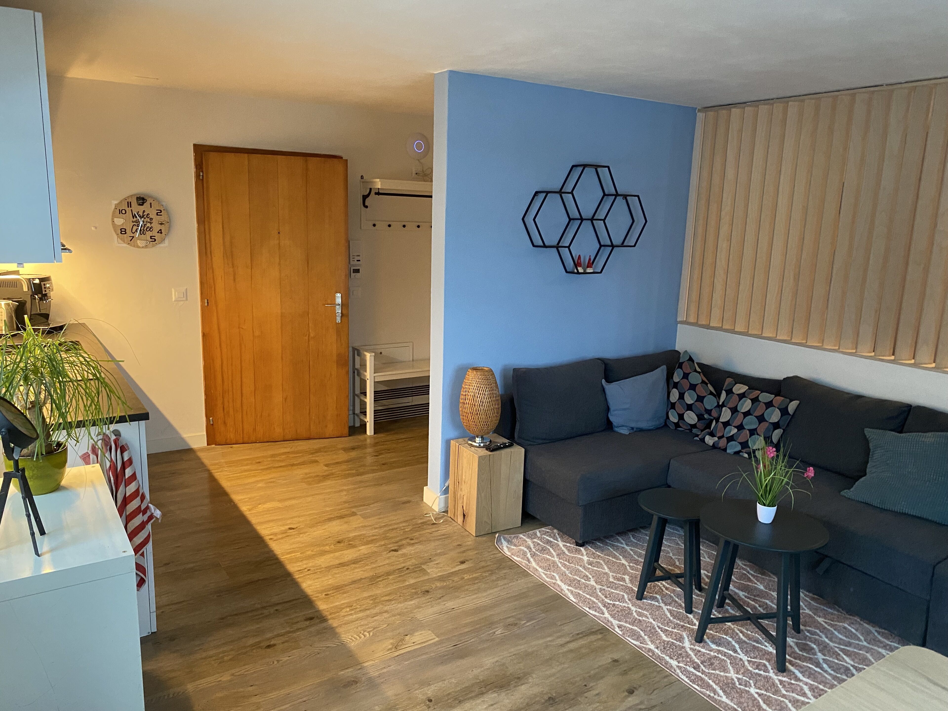 Ein modernes Wohnzimmer mit Holzboden, einem grauen Sofa, einem kleinen runden Tisch und einer dekorativen Wandgestaltung.
