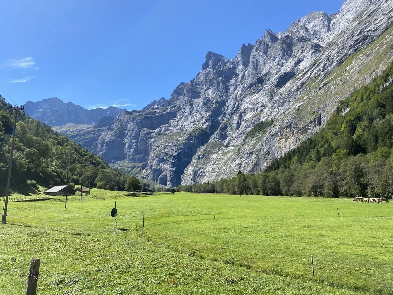 Eine gebirgige Landschaft mit einem grünen Feld, einem kleinen Gebäude und einem Zaun.