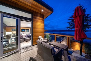 A modern outdoor deck with a wooden floor, wicker furniture, and a red umbrella.