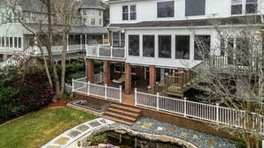 Une maison à deux étages avec un porche à l’avant, un petit jardin avec un étang et une clôture blanche.