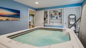 Une salle de spa dotée d’une grande baignoire, d’un tableau représentant un coucher de soleil sur une plage et d’une étagère contenant des articles de toilette.