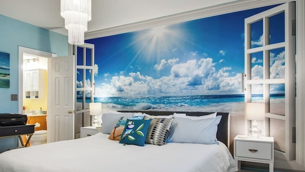 Une chambre avec un grand lit, du linge de lit blanc et une fresque murale représentant une plage.