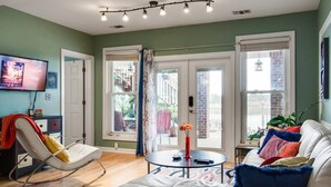 Un salon avec un canapé blanc, un fauteuil à bascule, une table basse et un téléviseur fixé au mur.
