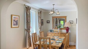 A dining area with a wooden table and chairs, a mirror above the table, and a window with curtains.