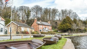 A row of traditional wooden boats lined up by a canal, with houses and a flagpole in the background.