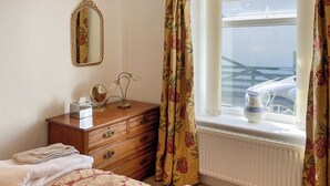 A bedroom with a bed, a dresser, a mirror, and a window with curtains.