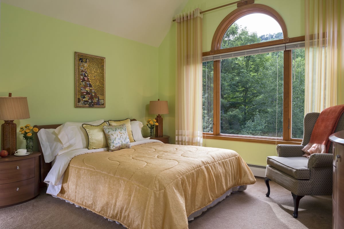 A bedroom with a large bed, two bedside tables with lamps, a chair, and a window with curtains.