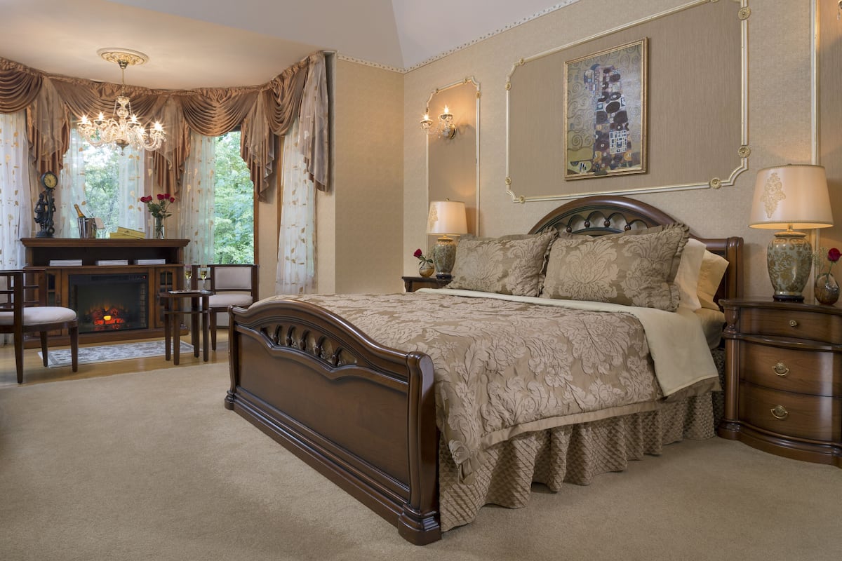 A bedroom with a large bed, a desk, and a fireplace.
