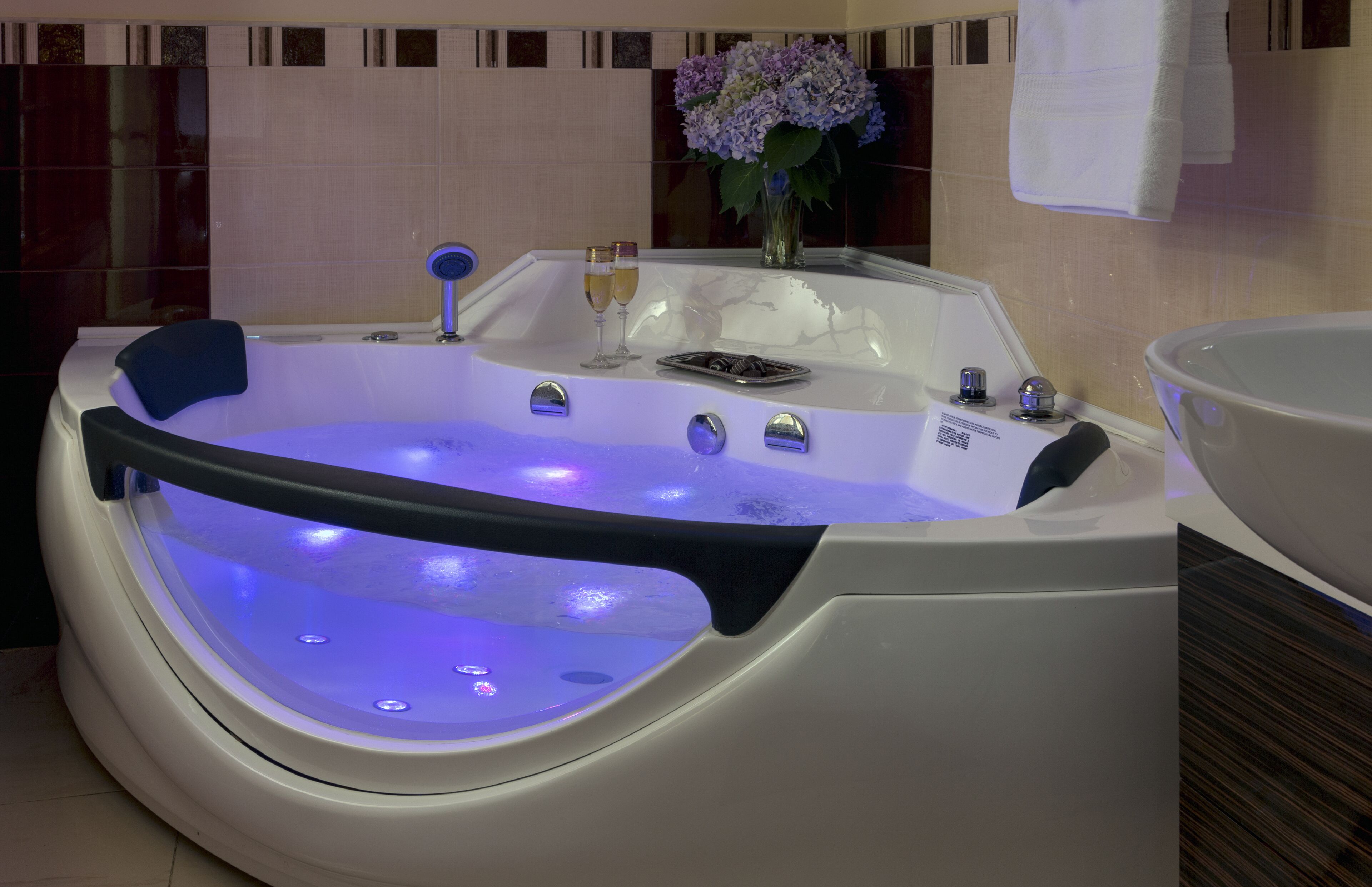 Een moderne badkamer met een ruime, verlichte whirlpool, een glas champagne en een bloemenvaas.