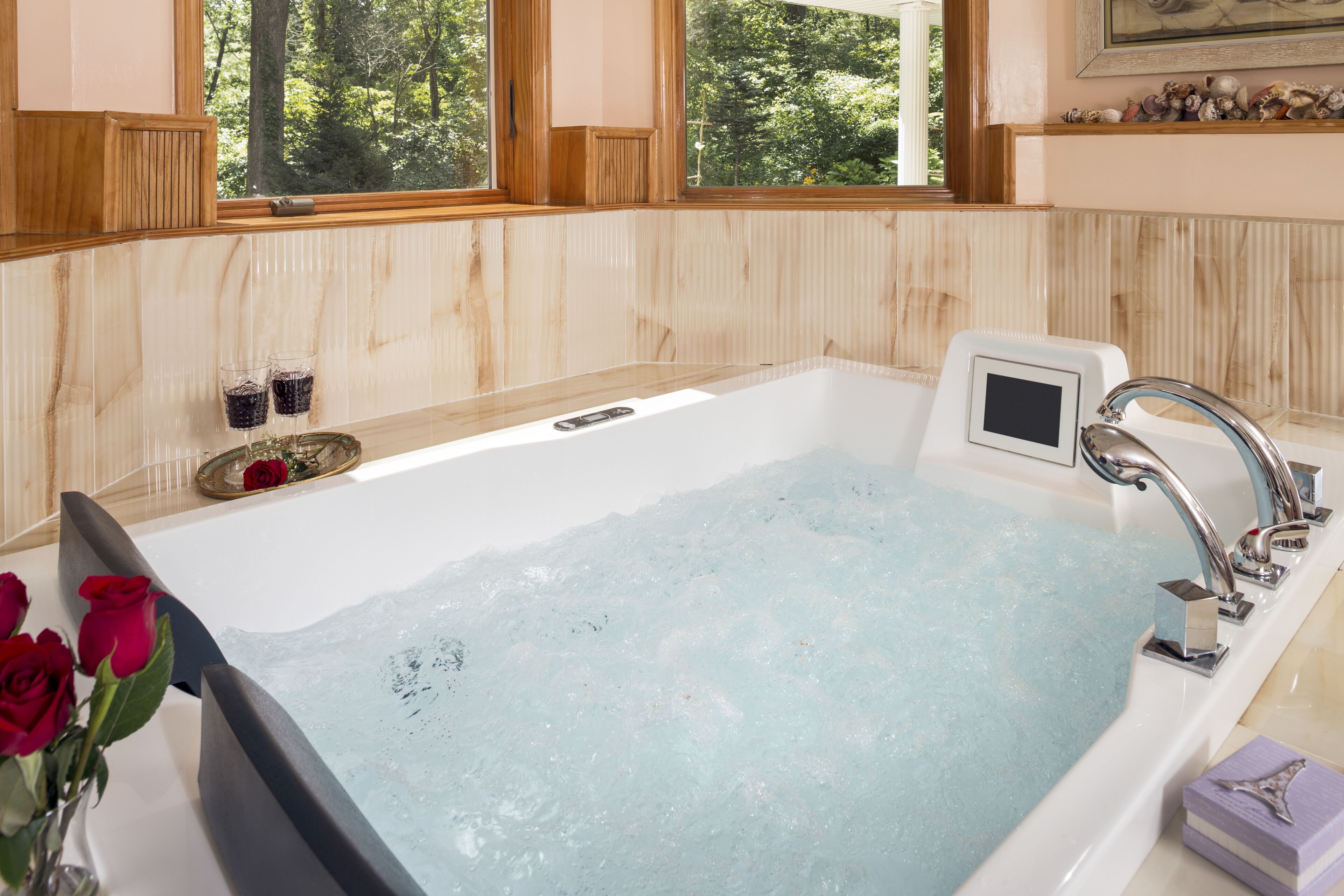 A bathtub with a digital interface, a window with a view of trees, and a vase with red roses.