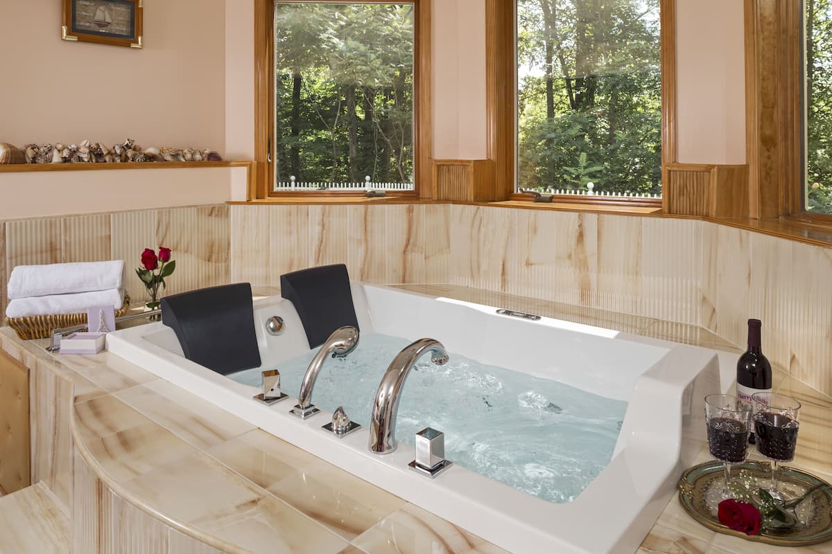 A large bathtub with two faucets, a glass of wine, and a rose on a tray.