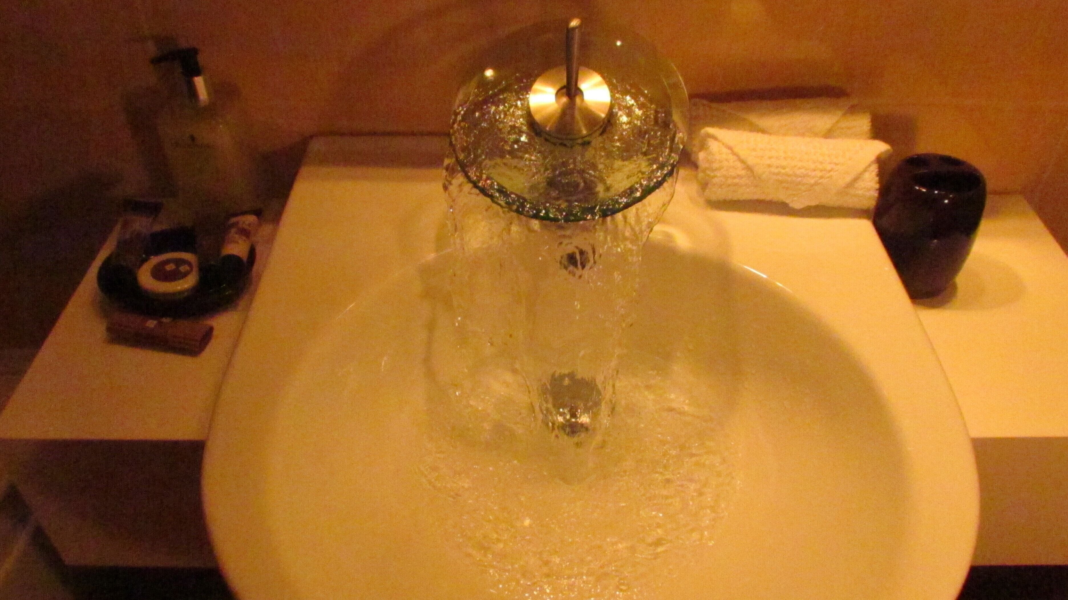A bathroom sink with running water, a towel, and a bottle.