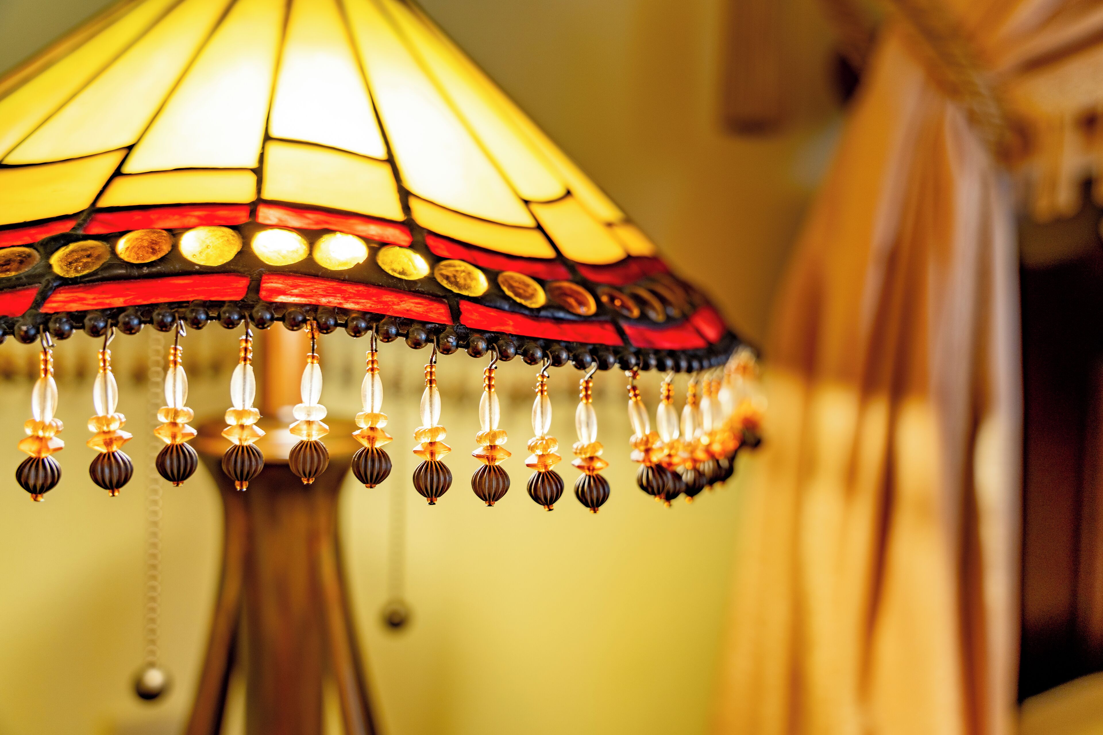 A close-up of a stained glass lamp with a wooden base and hanging beads.