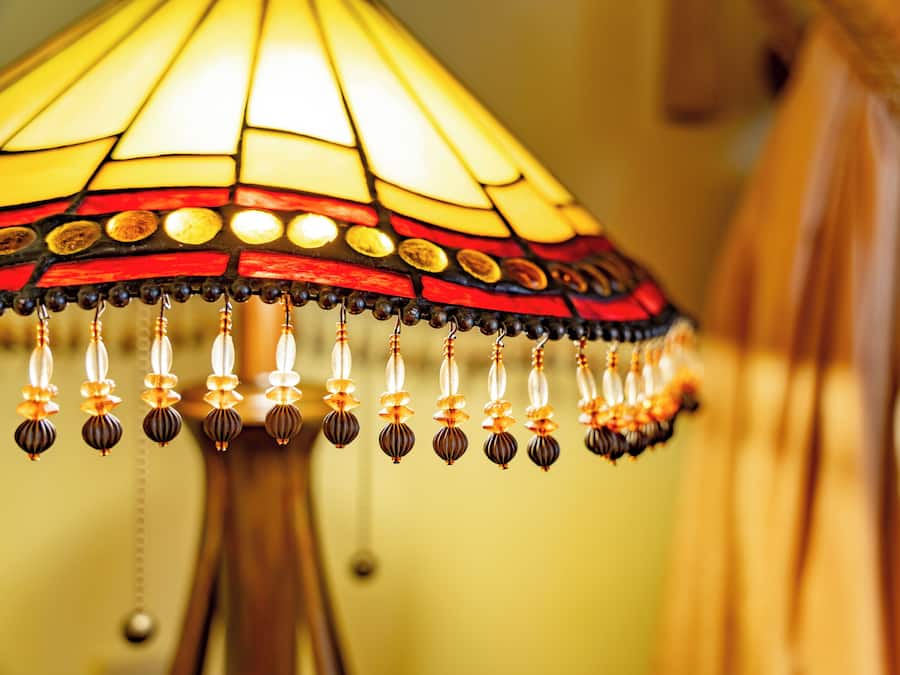 A close-up of a stained glass lamp with a wooden base and hanging beads.