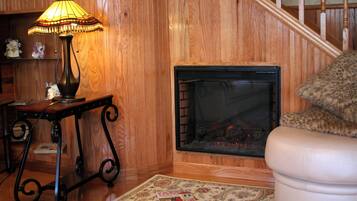 Un interior de madera con chimenea, una mesa con lámpara y una alfombra estampada.