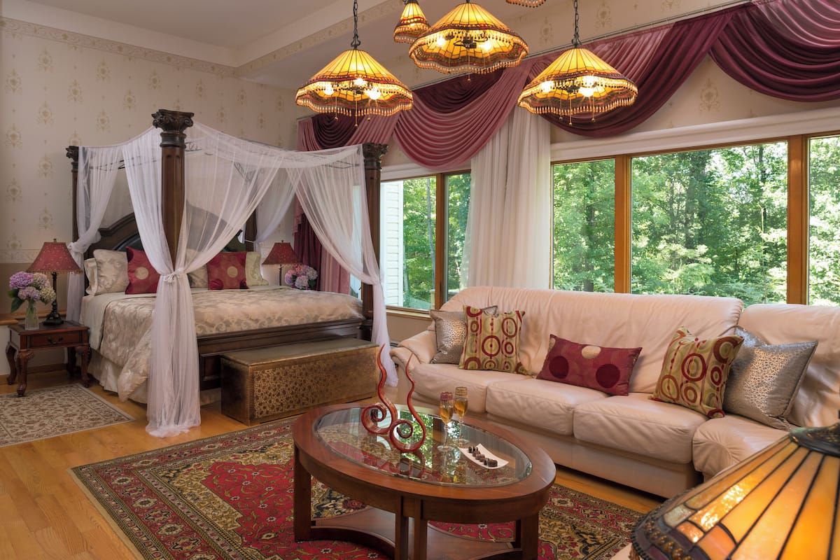 A bedroom with a four-poster bed, a sitting area with a sofa, and a glass coffee table.