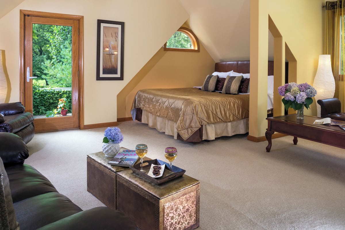 A bedroom with a bed, a nightstand, a coffee table, and a window with a view of greenery.