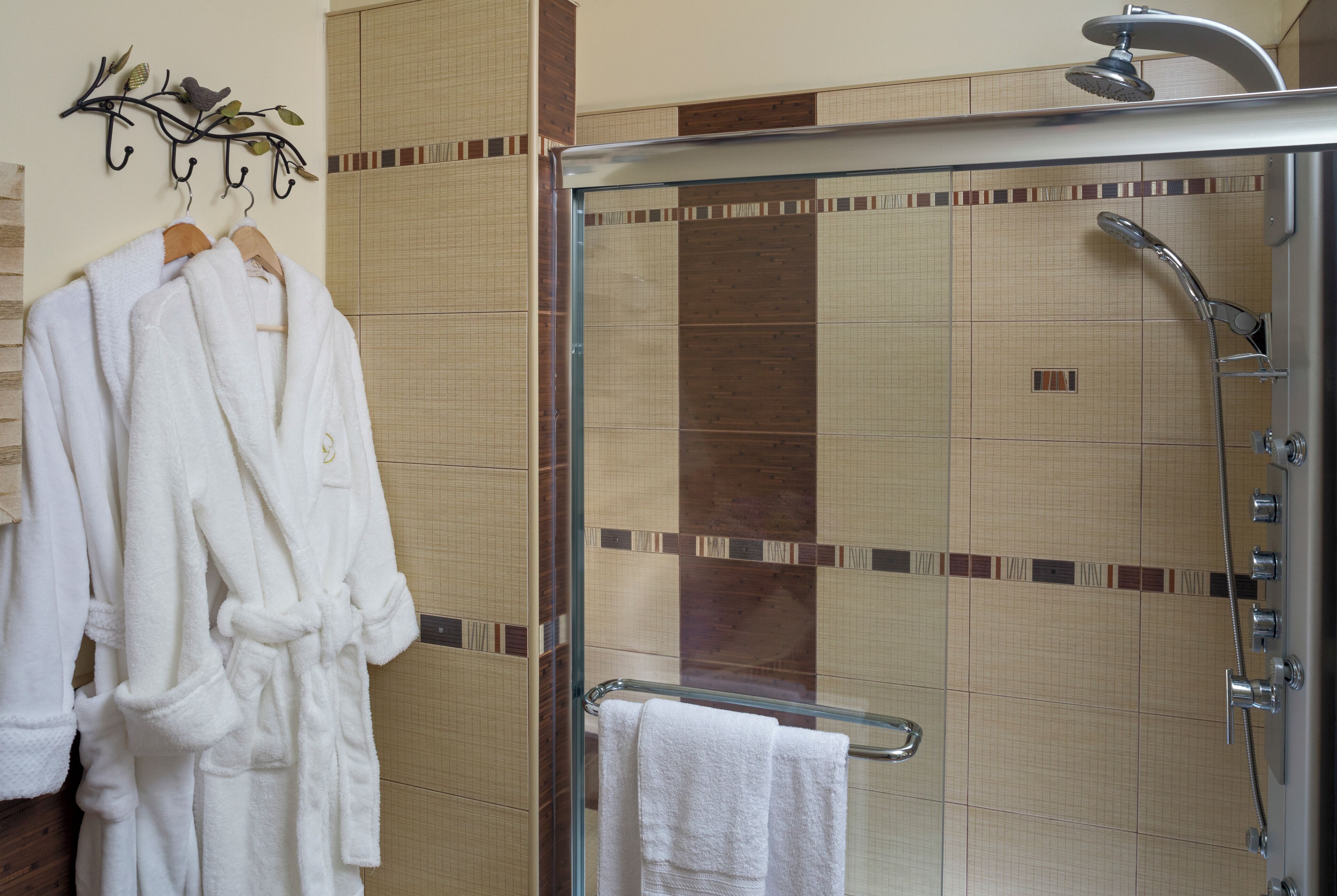 A bathroom with a glass-enclosed shower, a towel rack with white robes, and tiled walls.