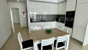 A modern kitchen with white cabinets, a wooden dining table, and four chairs. - Apartment with 2 bedrooms 100 meters from the beach / New (Quarteira)