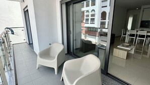 A balcony with two white plastic chairs, a glass door leading to a balcony with a view of a building, and a ceiling-mounted light fixture. - Apartment with 2 bedrooms 100 meters from the beach / New (Quarteira)