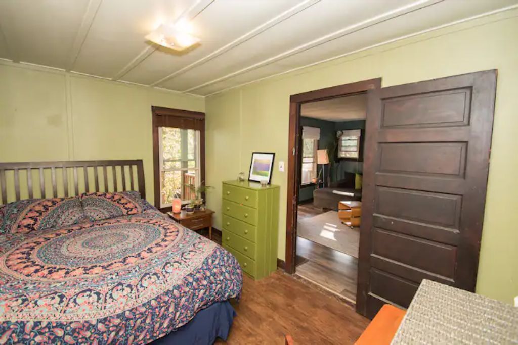 A bedroom with a large bed, a dresser, and a door leading to another room.