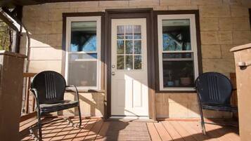 A wooden deck with a door and two windows, two chairs, and a rug leading to the door.