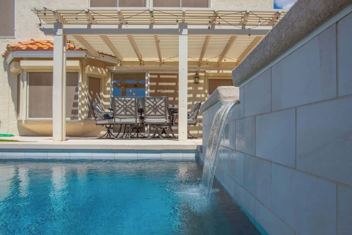 A swimming pool with a waterfall feature, outdoor seating, and a covered patio area.